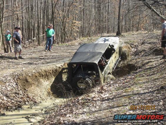 Off-road vehicle with a star graphic on the roof stuck in a muddy ditch on a wooded trail
