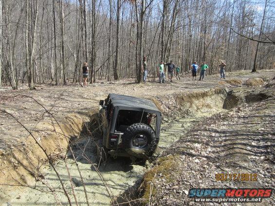 Black Jeep Wrangler navigating a muddy off-road trail with spectators watching