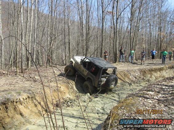 Off-road vehicle with a roll cage and spare tire on the back navigating a muddy ditch