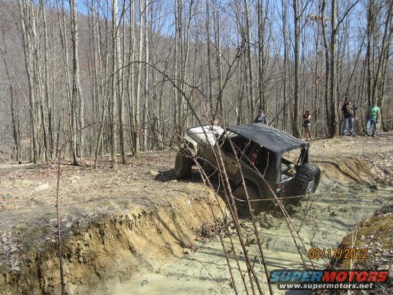 Off-road vehicle navigating a muddy ditch with people watching