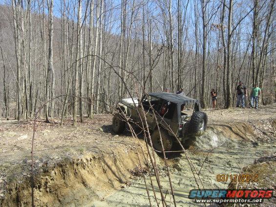 off-road vehicle navigating muddy trail in woods, people watching