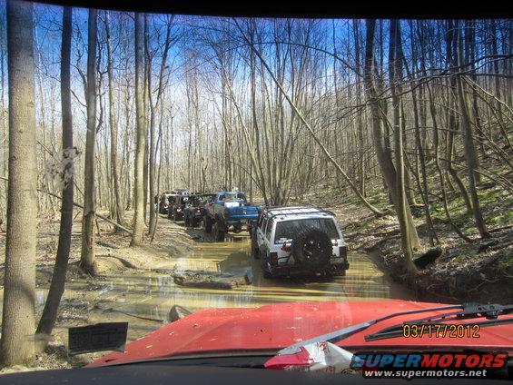 Multiple off-road vehicles navigate a muddy path in a forest. Date stamp reads 03/17/2012