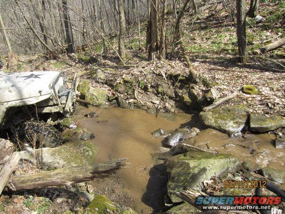 Off-road vehicle with a star on the hood stuck in a muddy creek bed in a wooded area
