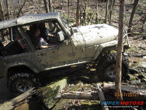 Mud-covered Jeep CJ-7 navigating rocky terrain with two occupants