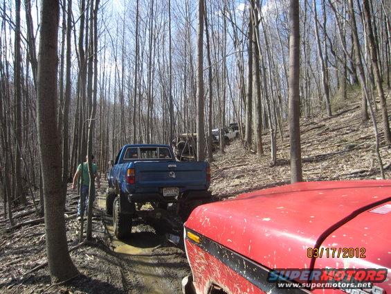 Red vehicle hood in foreground, blue pickup truck and other off-road vehicles on muddy forest trail. Date stamp 03/17/2012