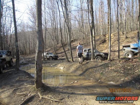 Off-road vehicles navigating a muddy trail in a forest, with a date stamp of 03/17/2012