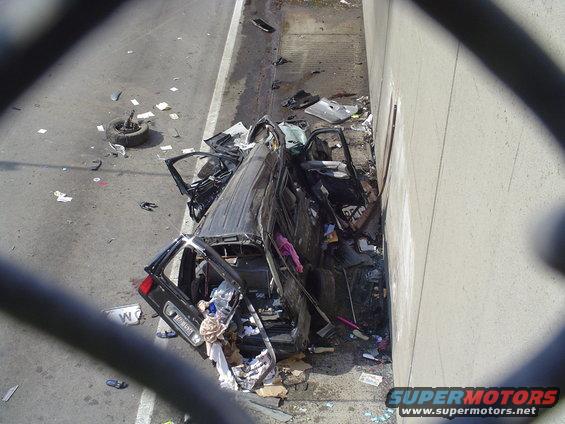 Wrecked black SUV crashed against a concrete wall, debris scattered on the road