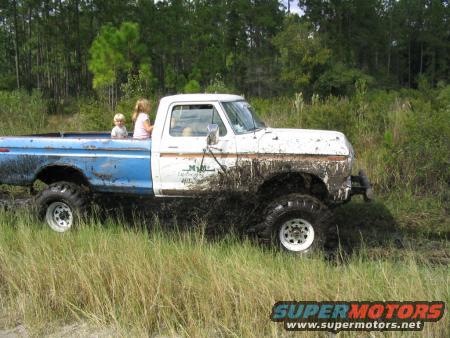 Mud-splattered white and blue pickup truck with two children in the bed, stuck in mud