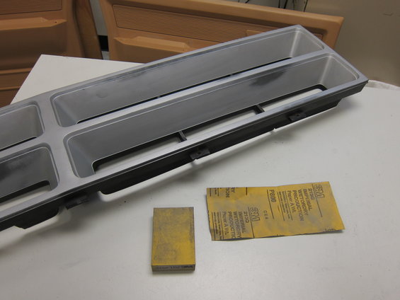 Car grille with two large rectangular openings and two smaller square openings, next to a sanding block and a sheet of P800 sandpaper