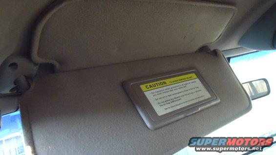 Tan sun visor with a yellow and black caution label, interior view
