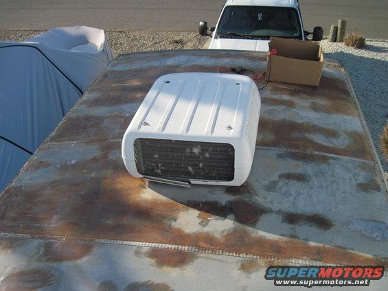 Trailer roof with white air conditioner unit and a white SUV in the background