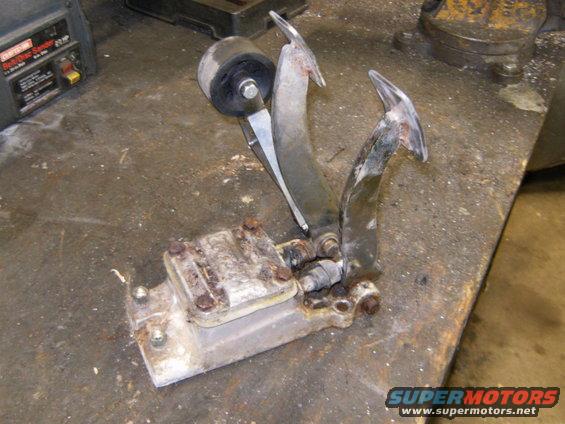Rusty brake and clutch pedals assembly with a rubber-tipped roller, mounted on a workbench