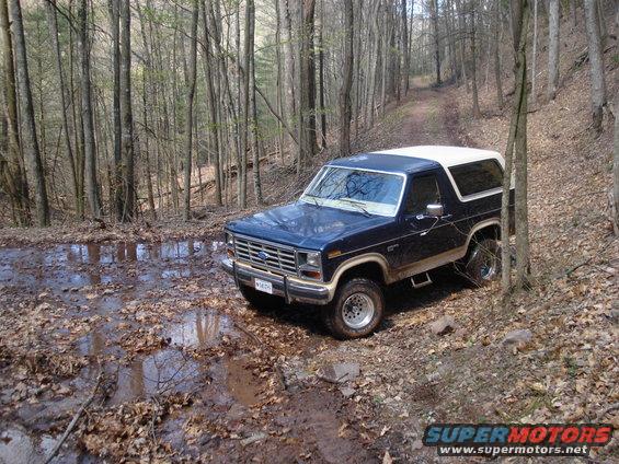 Dark blue and white 1985 Ford Bronco on a muddy forest road