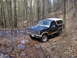 1985 Ford Bronco - A dark blue and white 1985 Ford Bronco navigates a muddy, wooded trail.