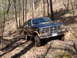 1985 Ford Bronco - Blue 1985 Ford Bronco navigating a rocky, wooded off-road path.
