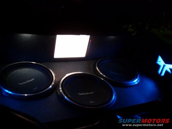 Car interior with three subwoofers and a glowing blue logo, dark setting