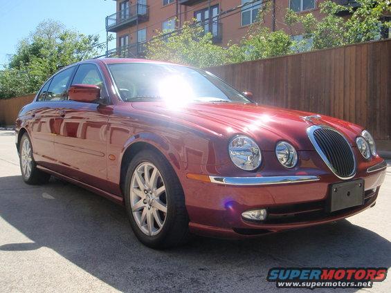 Red Jaguar S-Type sedan parked on pavement, front quarter view