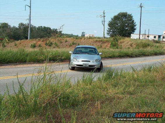 1998 Ford Taurus driving on a two-lane road with grassy shoulders