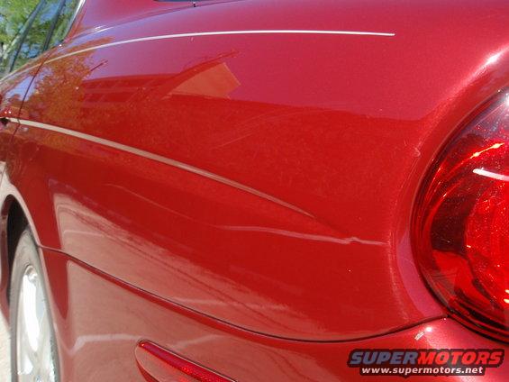Red sedan's rear quarter panel with a pinstripe and some scratches. Tail light visible