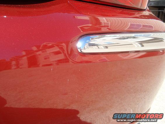 Close-up of a red car's rear bumper with a chrome accent strip