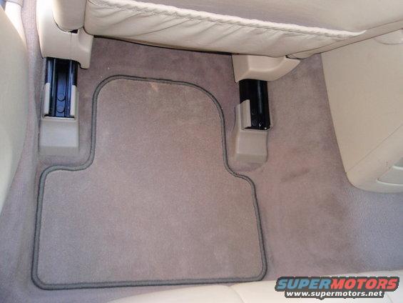 Car interior floor mat with gray piping. Visible seat rails and beige upholstery