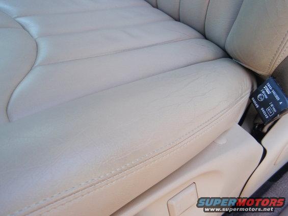 Close-up of a tan leather car seat with stitching detail. A seatbelt buckle is visible on the right