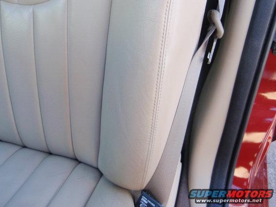 Beige leather car seat with stitching and a gray seatbelt. Red exterior visible on the right
