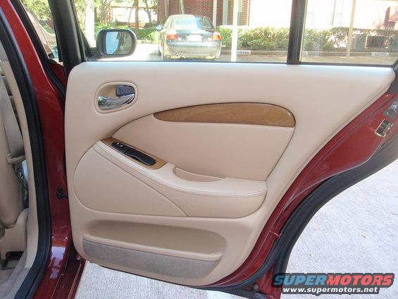 Interior door panel of a red car with tan upholstery and wood trim. Another car is visible through the window