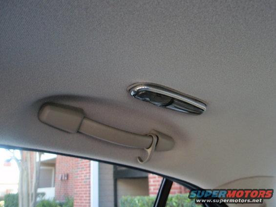 Car interior ceiling with grab handle and light fixture. Building visible through window