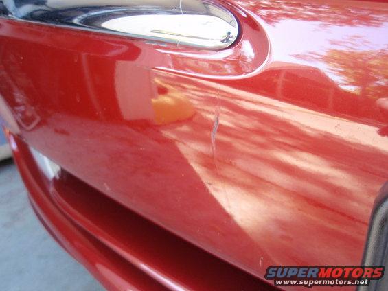 Red car fender with chrome trim and a scratch. Supermotors.net logo visible