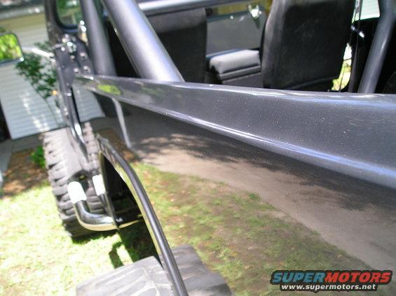 Dark grey SUV interior with roll cage, black seats, and a close-up of the side panel. Tires and grass visible