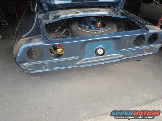 Blue car's rear with trunk open, showing spare tire and wiring. Taillight housings are empty