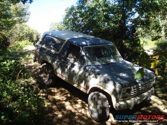 1985 Ford Bronco on a dirt trail, front 3/4 view, covered in dust