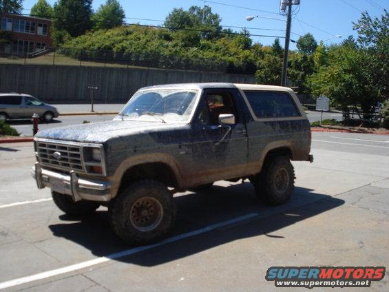 Muddy Ford Bronco parked in a lot. It has a two-tone paint job and off-road tires
