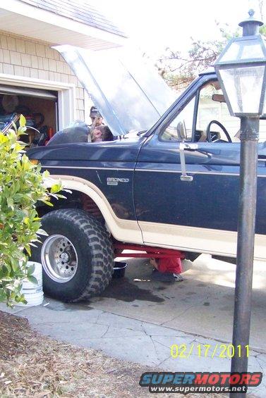 Dark blue and tan Ford Bronco with hood open, undergoing maintenance