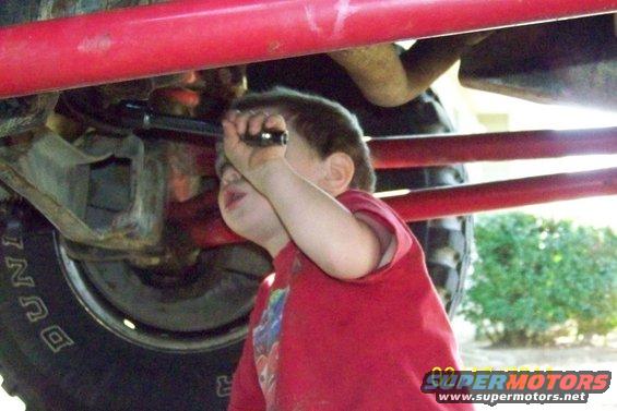 Child in red shirt looking at the suspension and tire of a vehicle