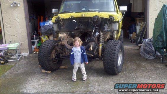 kid in front of yellow truck with front end removed, lifted suspension, big tires
