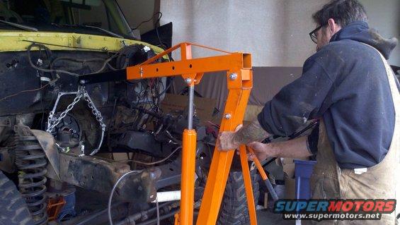 Engine hoist lifting the engine out of a yellow vehicle's engine bay