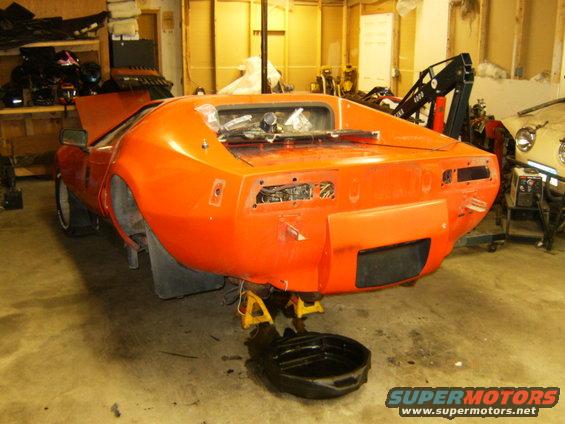 Orange sports car rear view, on jack stands with oil pan below