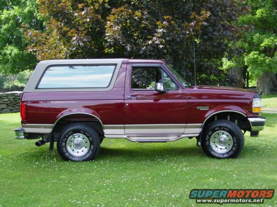 Maroon Ford Bronco with tan top, side view, parked on grass