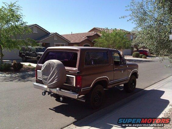 Brown Ford Bronco with a spare tire cover on the rear, parked on a street in front of houses