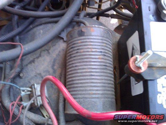 Engine bay with battery, hoses, and a ribbed metal canister