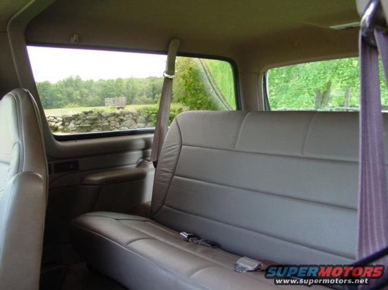 Back seat and side window view from inside an SUV, looking out at a stone wall and trees