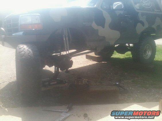 1995 Ford Bronco with camouflage paint, lifted suspension, and front wheel removed for service