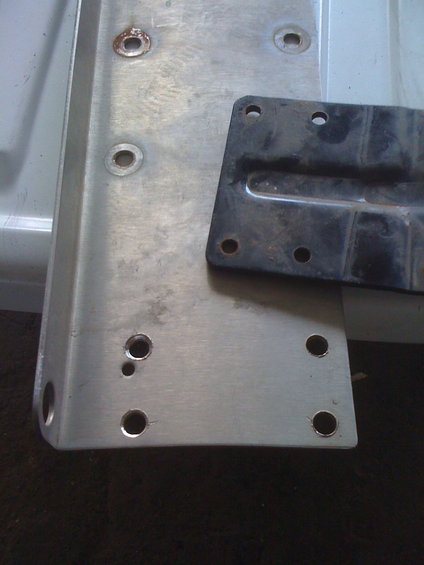 Close-up of a metal bracket with holes, next to a black mounting plate