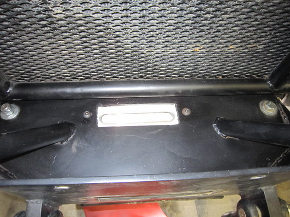 Close-up of a winch mounting plate with a rectangular cutout, bolted to a vehicle's frame below the grille