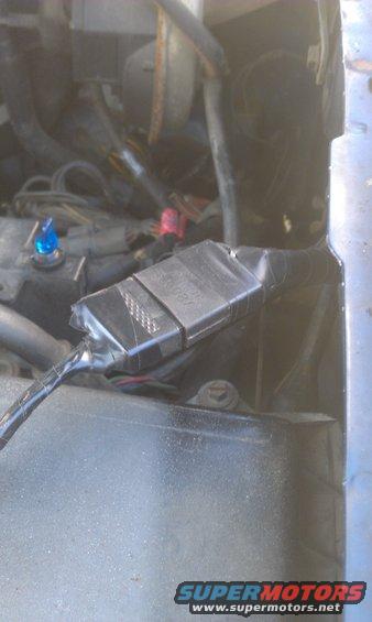 Engine bay wiring harness with a black plastic connector taped up. Blue indicator light visible