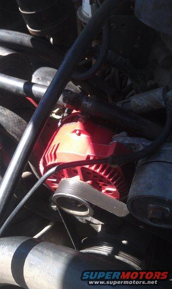 Close-up of a red alternator with a black belt in an engine bay