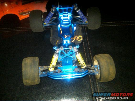 Blue remote control car chassis with yellow shocks. Orange RC car body in background