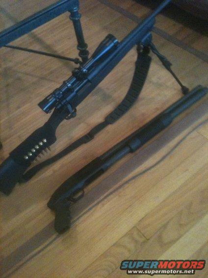 Two black firearms, a scoped rifle with bipod and a shotgun, rest on a wooden floor